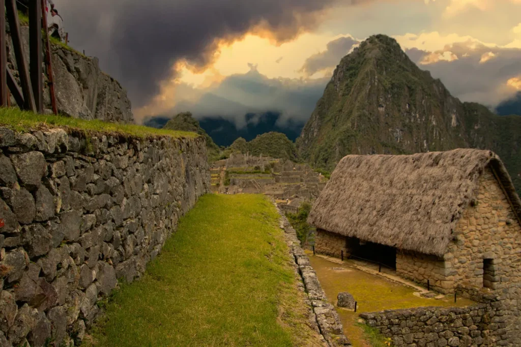 Trilha de pedra com gramado entre muros incas em Cusco e Machu Picchu, com montanhas dos Andes ao fundo.