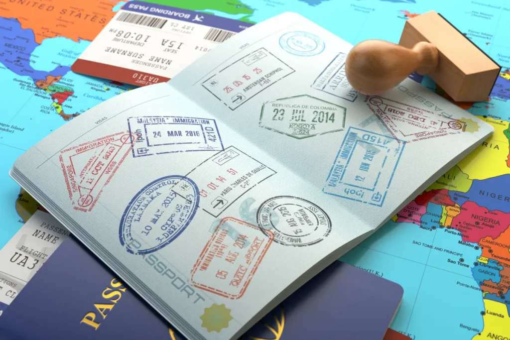 Passaporte aberto com vários carimbos de imigração sobre um mapa colorido, acompanhado de um carimbo de madeira ao lado.