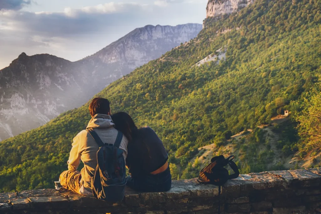 viajante sentado em uma pedra observando montanhas cobertas por vegetação