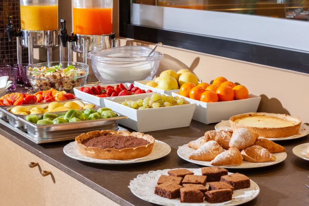 Buffet de café da manhã com pães, frutas, sucos e pratos quentes organizado sobre uma mesa em restaurante de hotel.