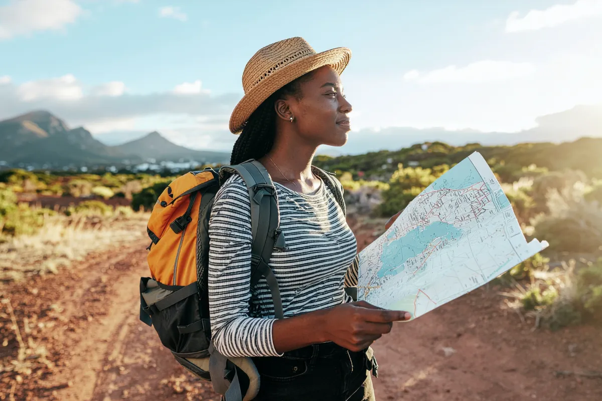 viajante com chapéu e mochila segurando um mapa enquanto observa uma paisagem montanhosa ao fundo