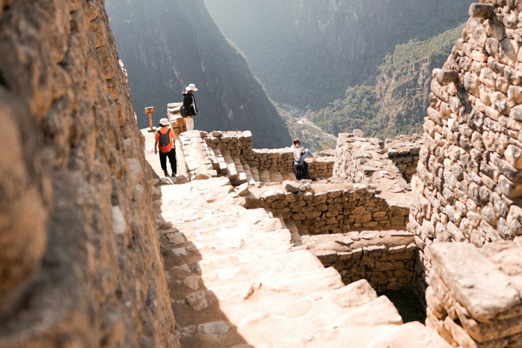Turistas caminhando por escadarias de pedra nas ruínas de Machu Picchu, no Peru.