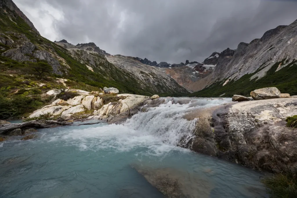 Lagoa de água azul cercada por rochas e montanhas altas em uma paisagem natural da Cordilheira dos Andes.