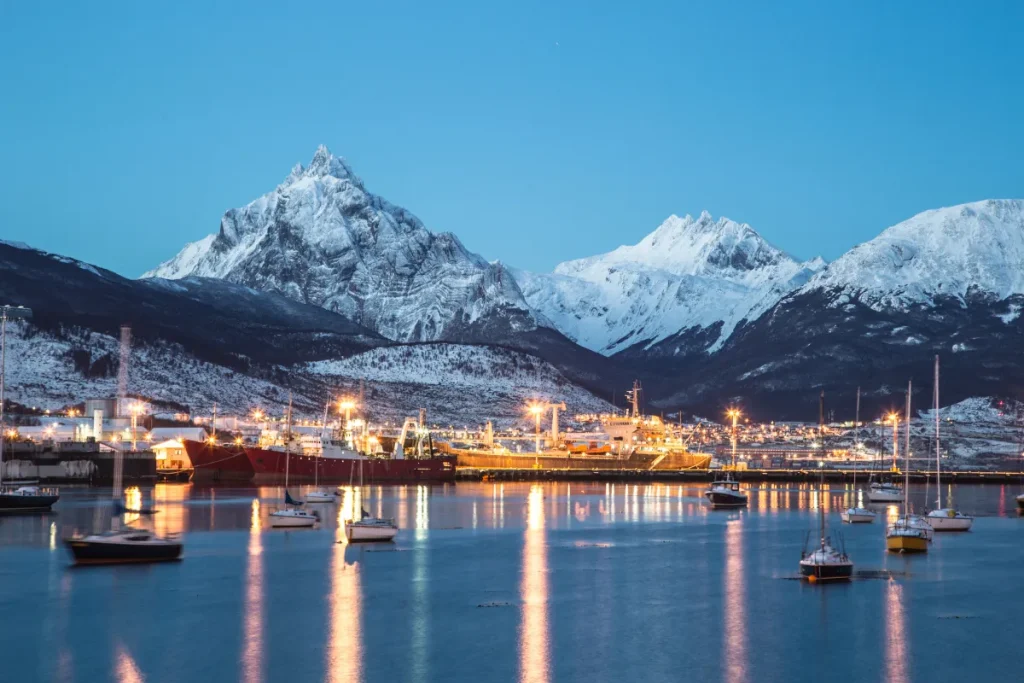 Vista da cidade de Ushuaia com barcos no mar e montanhas nevadas ao fundo na Patagônia argentina.
