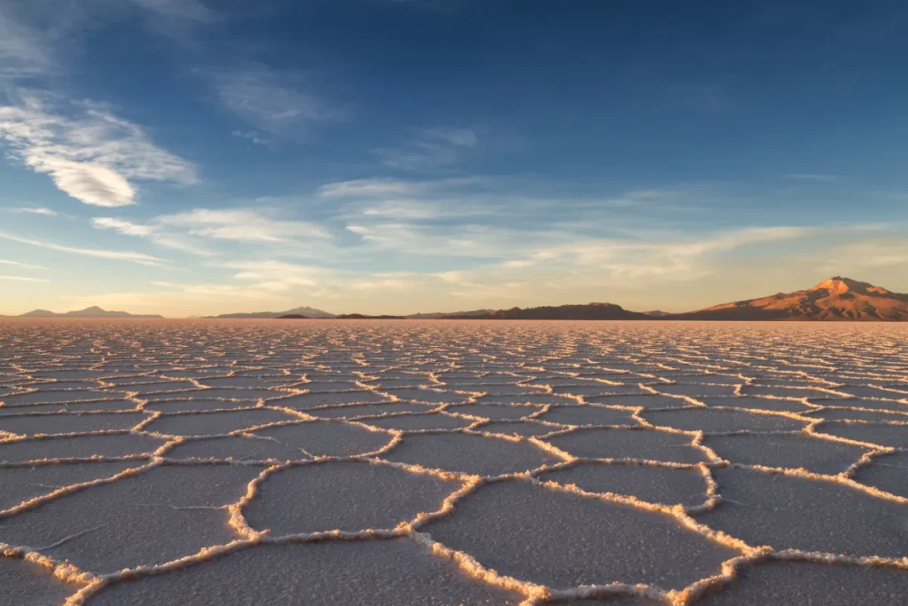 Superfície do Salar de Uyuni com placas de sal formando padrões geométricos sob céu azul na Bolívia.