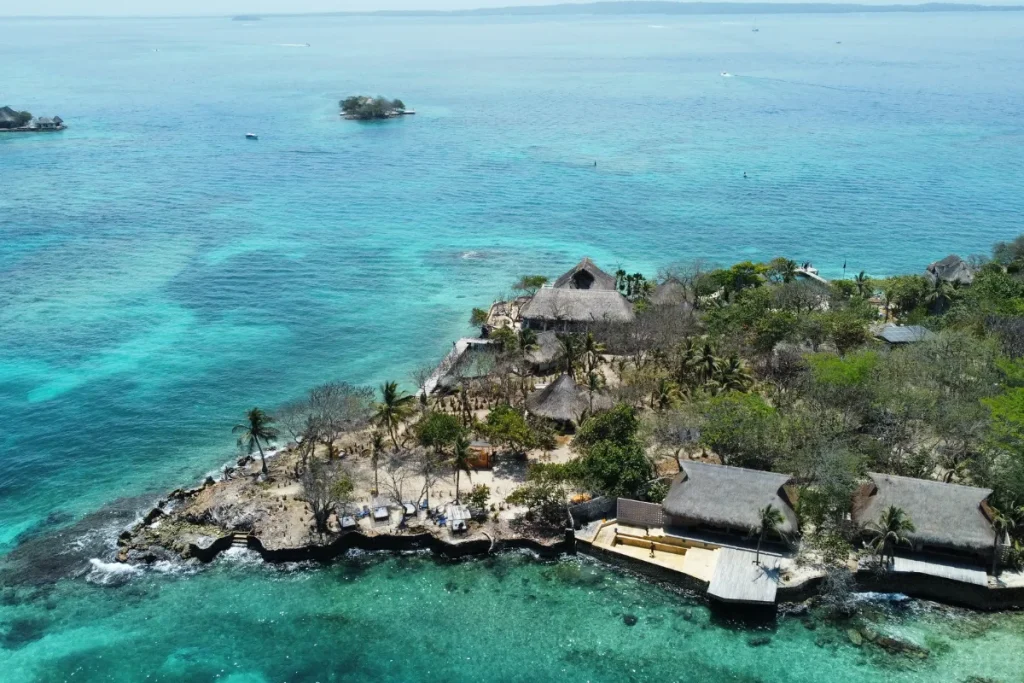 Pequena ilha rochosa com vegetação e construções cercada por mar azul-turquesa na costa do Caribe colombiano.