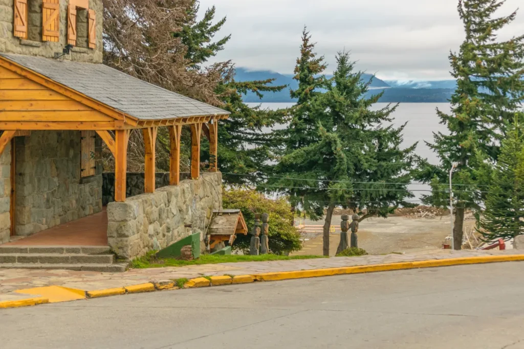 Casa de estilo alpino em Bariloche com árvores ao redor e vista para o lago Nahuel Huapi ao fundo.