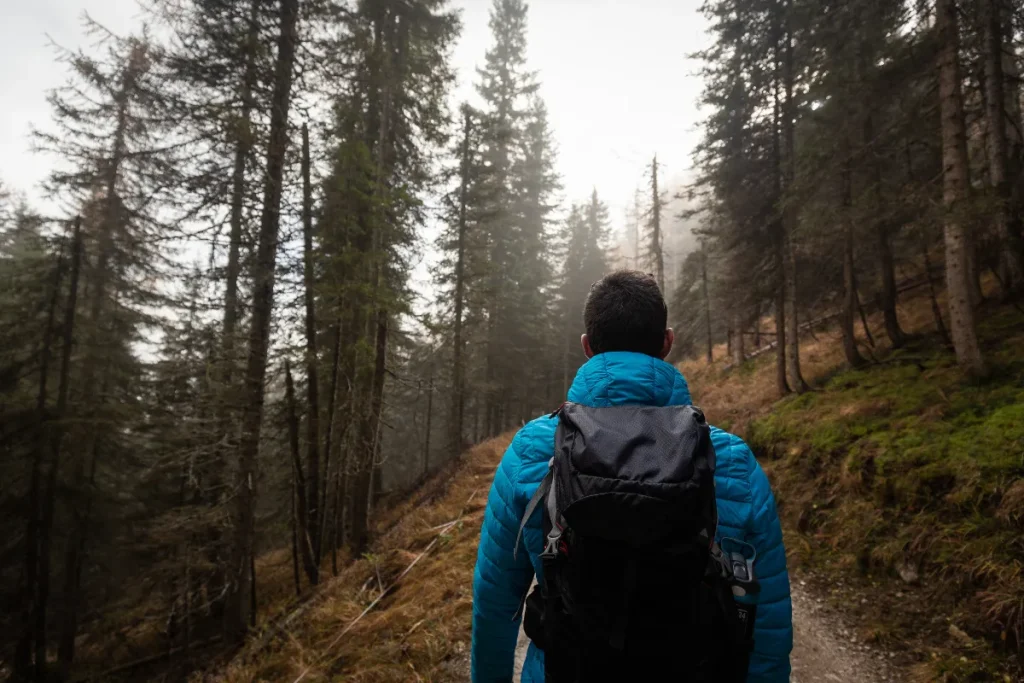 Homem com mochila caminhando por trilha em floresta montanhosa com neblina ao fundo em um Circuito Andino confortável e seguro.