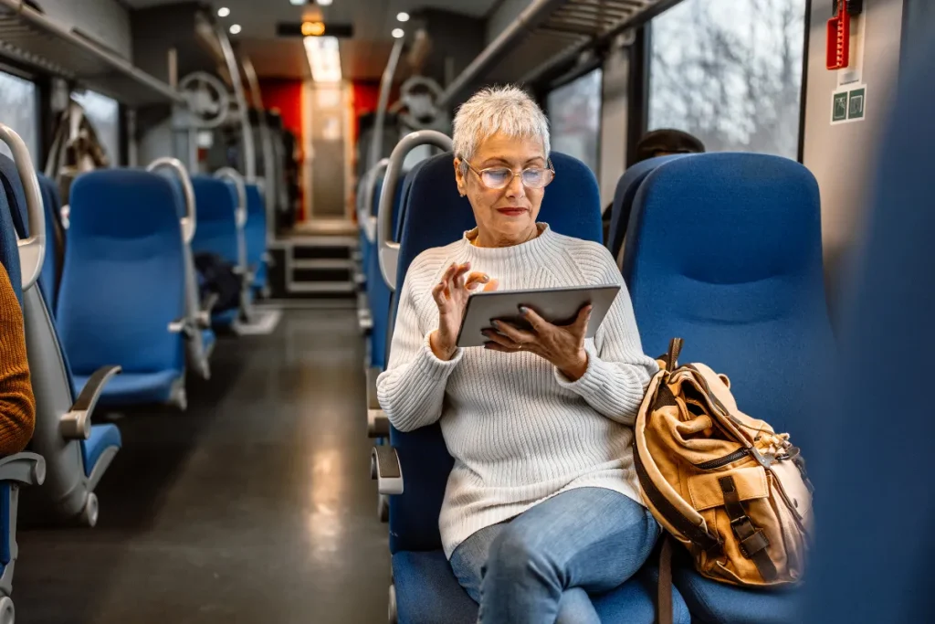 Mulher idosa sentada em trem utilizando tablet durante Circuito Andino para 60+.