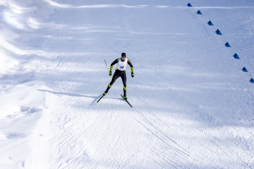 Atleta praticando esqui em uma pista coberta de neve usando roupa esportiva e bastões de esqui.