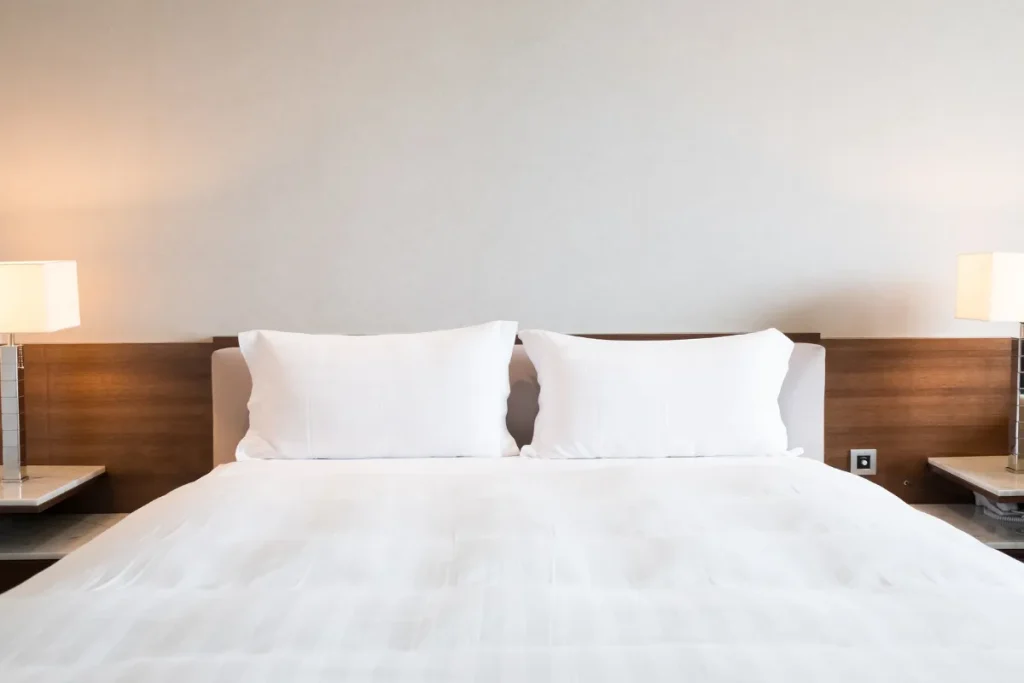 Quarto de hotel com cama de casal arrumada e duas luminárias laterais