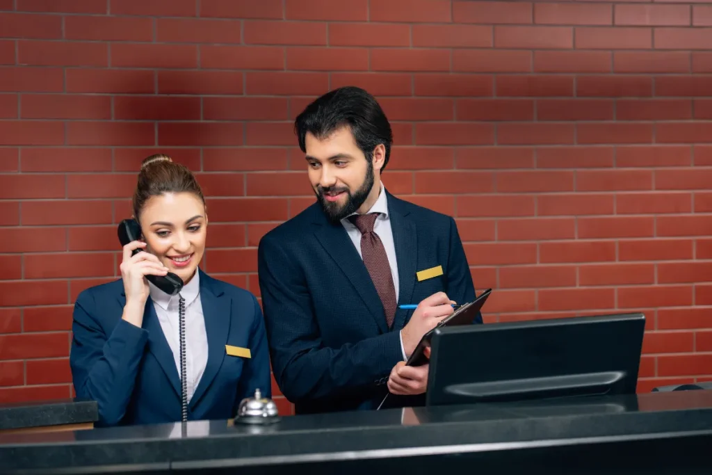 Funcionária de um dos hotéis do Circuito Andino atendendo ao telefone na recepção enquanto colega anota informações em prancheta.