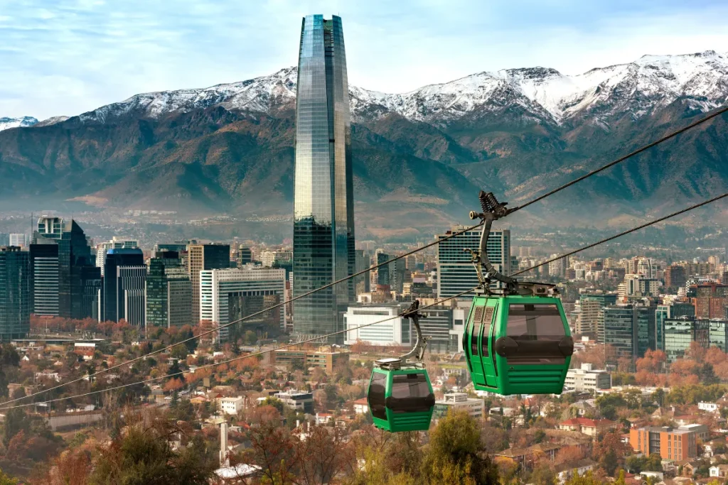 Teleférico verde passando sobre a cidade de Santiago com prédios e montanhas nevadas ao fundo