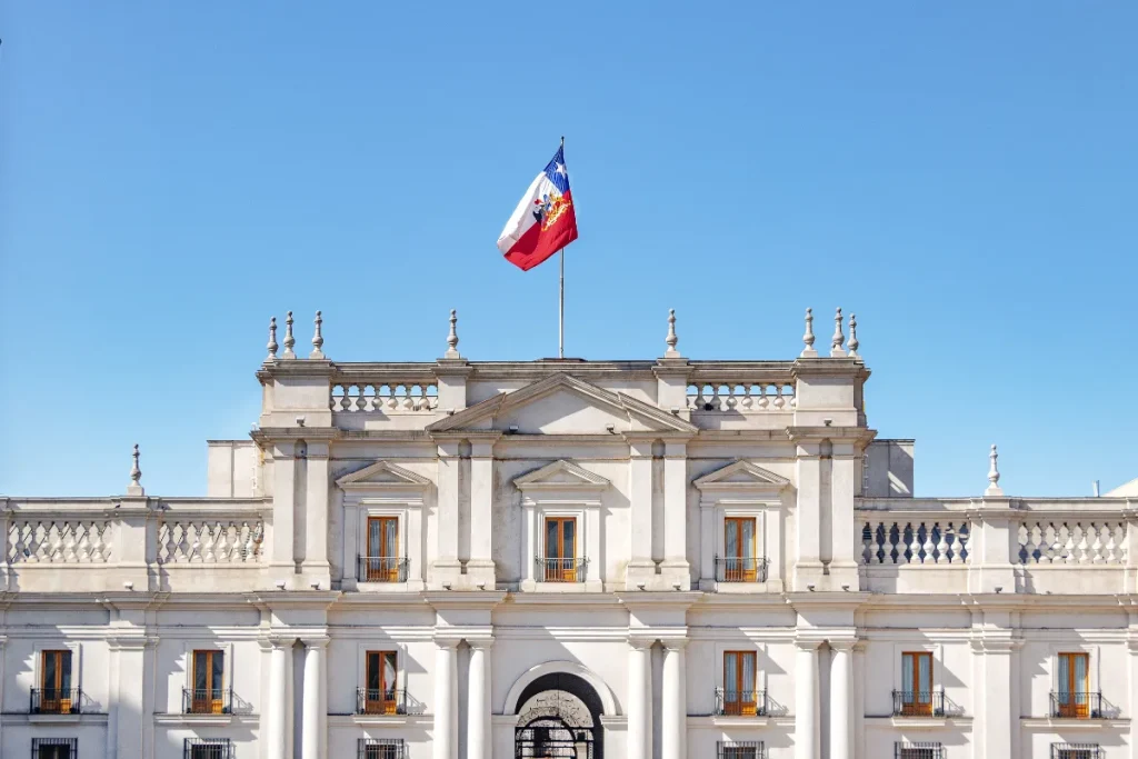 Fachada do Palácio La Moneda com bandeira do Chile no topo e céu azul ao fundo