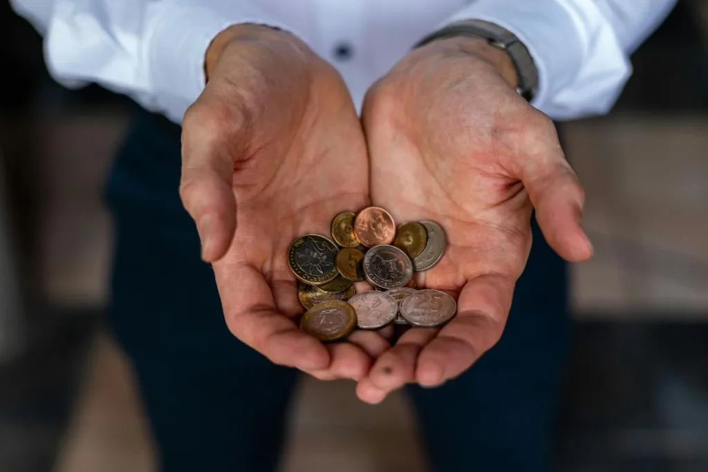 Moeda em Bariloche. Mãos abertas exibindo moedas de peso argentino de diferentes valores