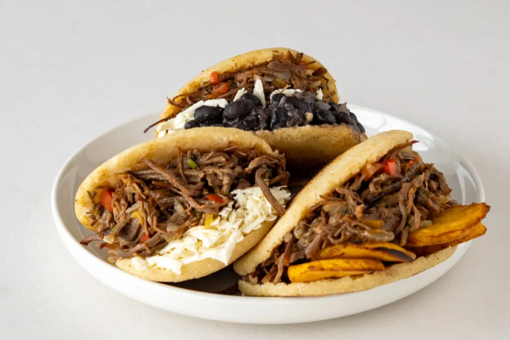 Arepas recheadas com carne desfiada, queijo, feijão e banana-da-terra, mostrando versões típicas da gastronomia latina.