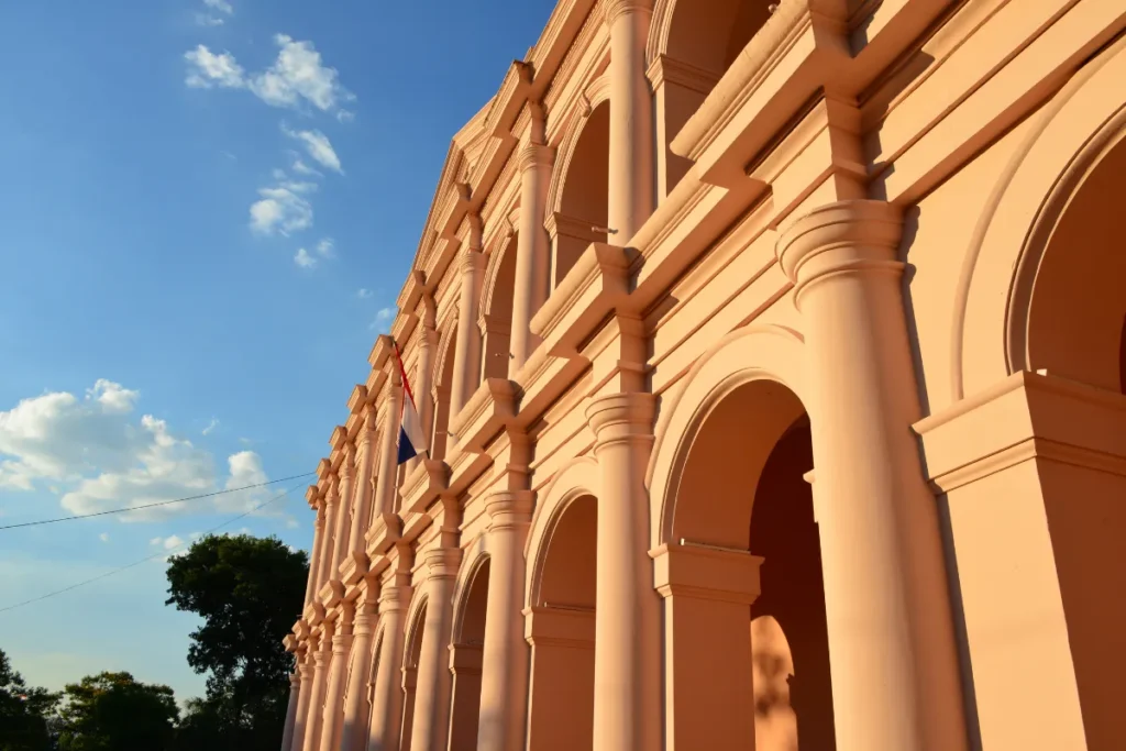 Fachada com arcos e colunas do Palácio de los López sob céu azul, representando o patrimônio histórico de Assunção.