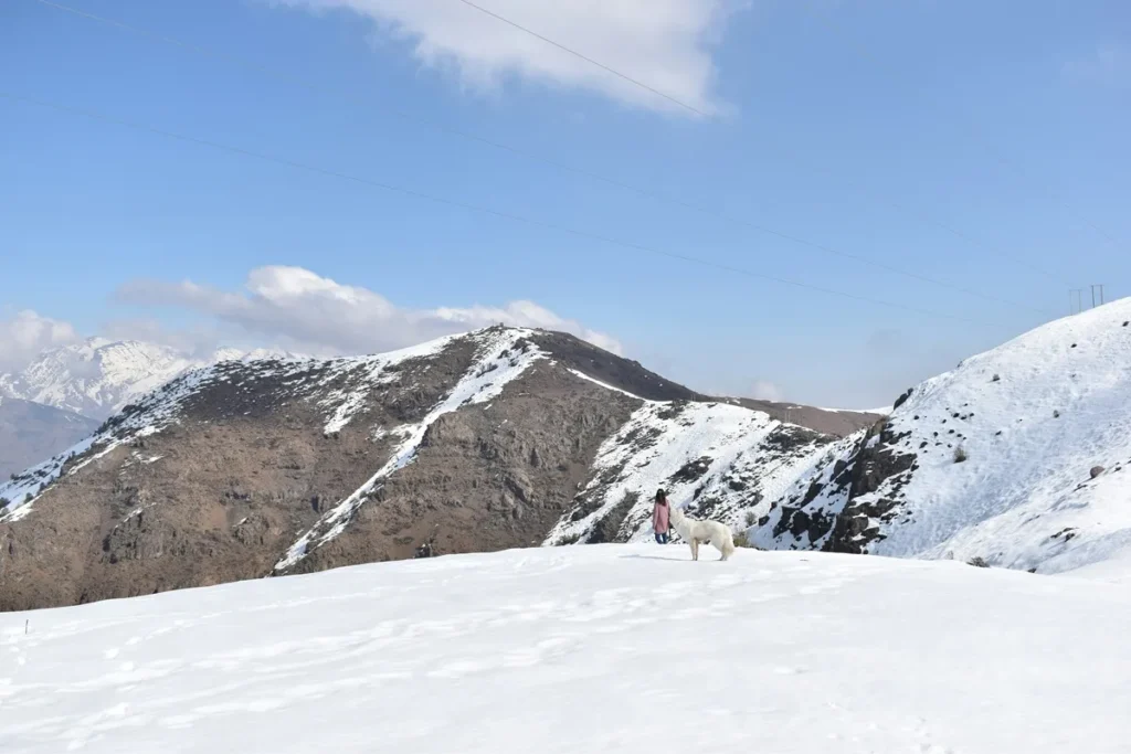 Clima em Santiago: qual a melhor época para conhecer a cidade? Montanhas nevadas nos Andes perto de Santiago do Chile com turista caminhando na neve.