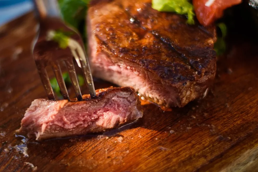 Bife suculento ao ponto sendo cortado com garfo mostrando interior macio e rosado