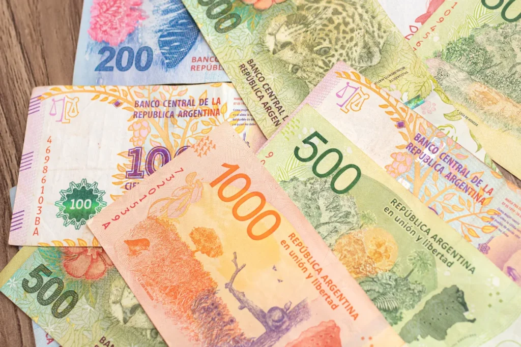 Notas de pesos argentinos de diferentes valores espalhadas sobre mesa, mostrando a moeda usada por turistas em Bariloche.