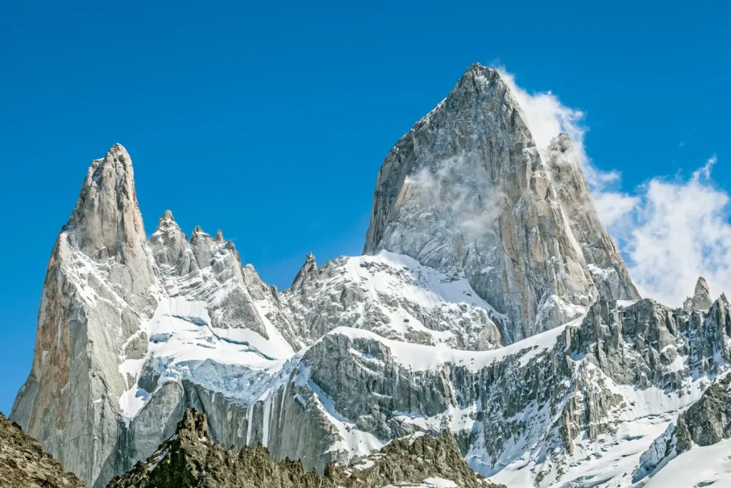 Montanhas nevadas no Parque Nacional Los Glaciares com picos rochosos sob céu azul na Patagônia Argentina.