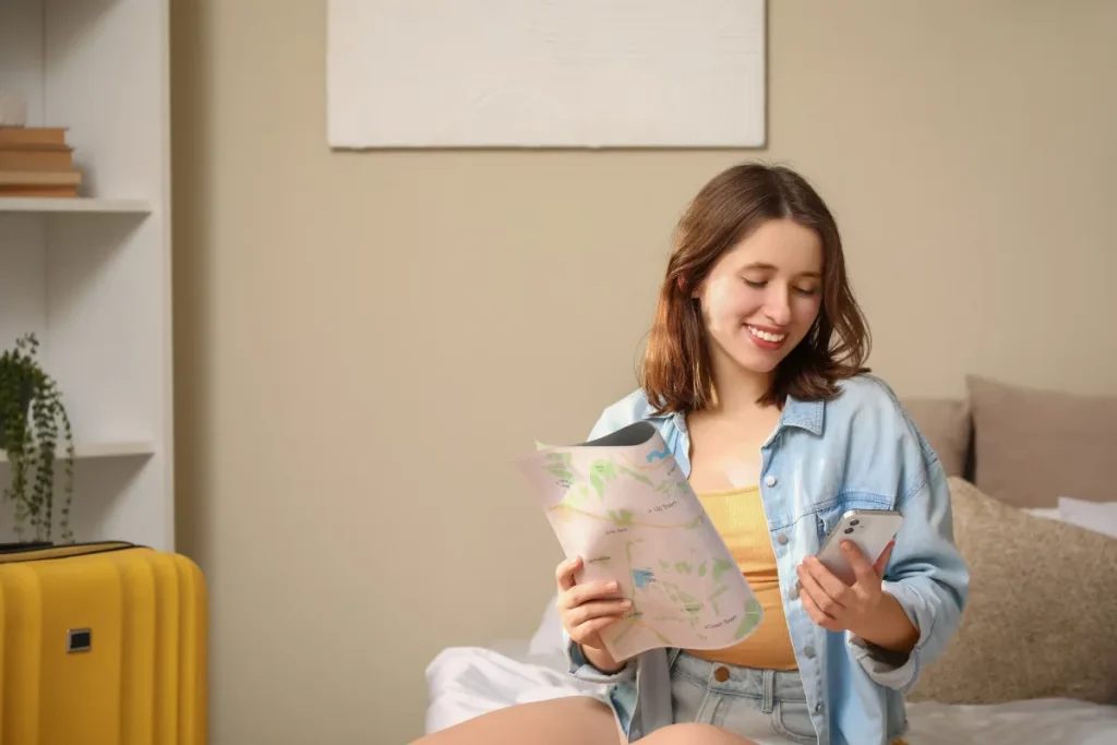 Quanto custa viajar para Bariloche: valores de hotel, comida e passeios em reais Mulher segurando mapa e olhando celular enquanto organiza viagem dentro de casa