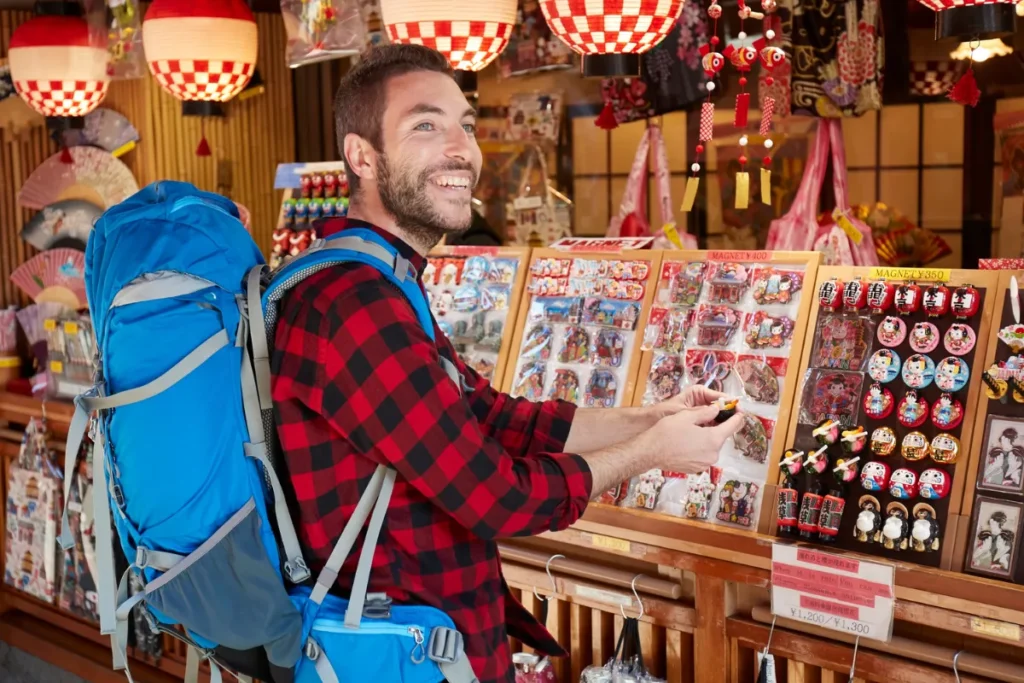 Turista com mochila fazendo compras em loja de lembranças, destacando cuidados com pertences em viagens.