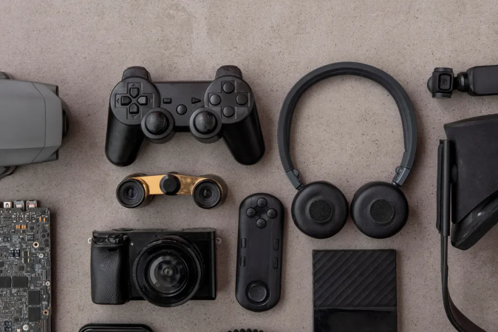 Câmera, controle de videogame, headset e gadgets tecnológicos organizados sobre superfície cinza.