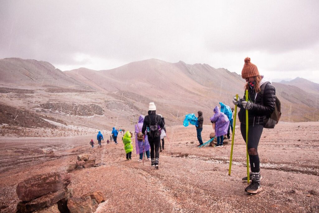 Grupo de pessoas vestindo capas de chuva caminhando em uma trilha montanhosa sob condições climáticas adversas.