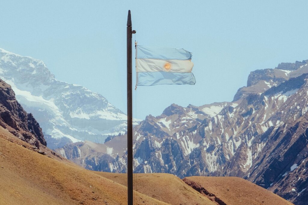 Bandeira da Argentina hasteada diante de montanhas nevadas da Cordilheira dos Andes.
