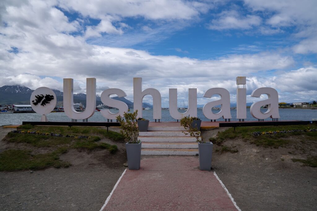 Letreiro turístico de Ushuaia com o Canal de Beagle e montanhas ao fundo na Argentina.