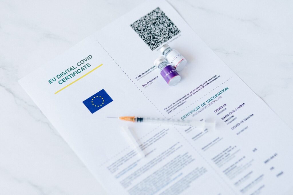 Certificado digital de vacinação com QR Code, frascos de vacina e seringa, representando a conferência de requisitos sanitários antes de uma viagem internacional.