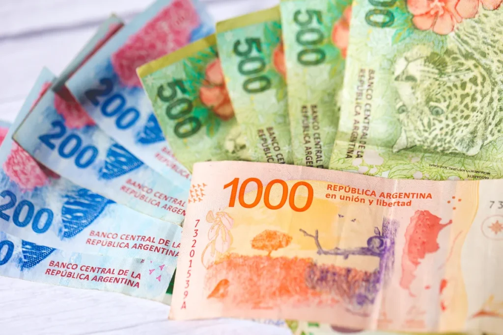 Conjunto de cédulas de pesos argentinos de diferentes valores espalhadas sobre uma superfície clara, úteis para turistas.