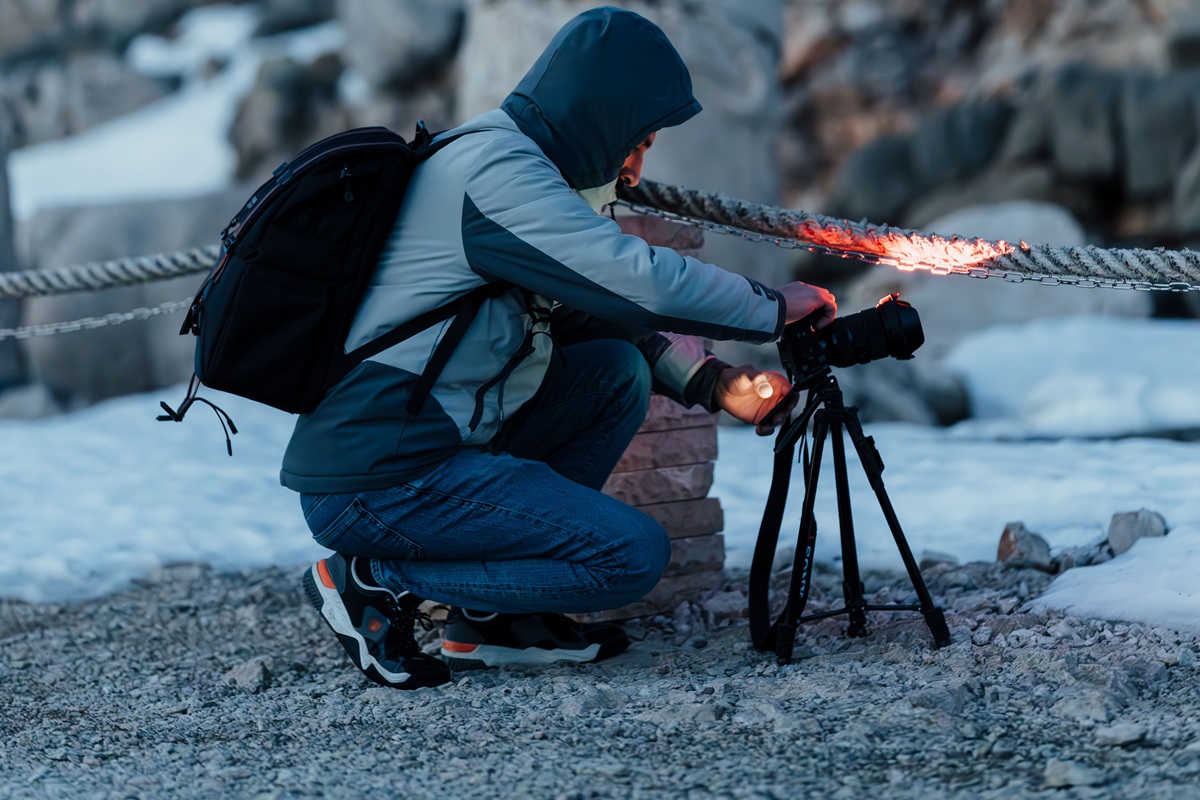 Fotógrafo ajustando uma câmera em tripé em uma montanha coberta de neve ao amanhecer.