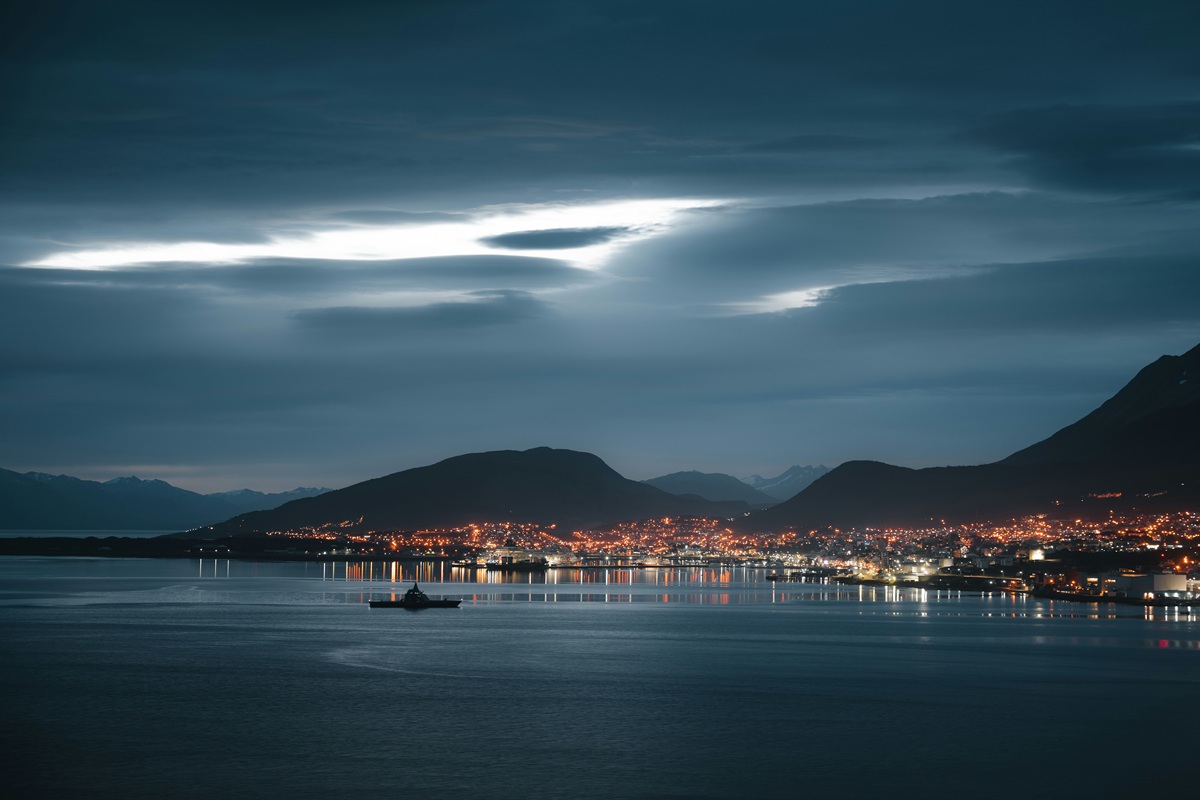 Vista noturna de Ushuaia a partir da água, com luzes urbanas, montanhas e o Canal de Beagle.