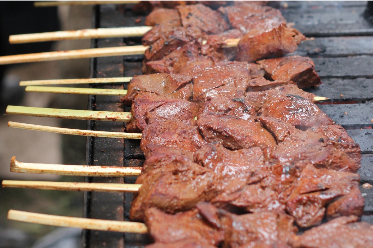 Anticuchos sendo preparados e pincelados sobre uma grelha em Lima