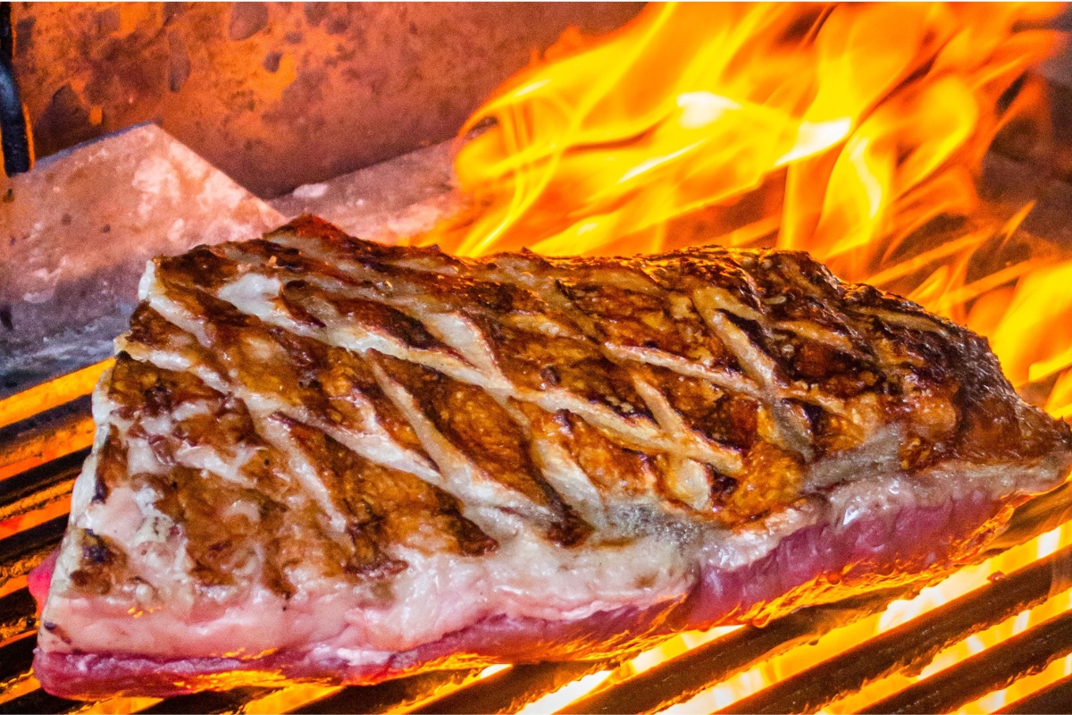 Carne sendo grelhada sobre chama aberta em uma cozinha profissional