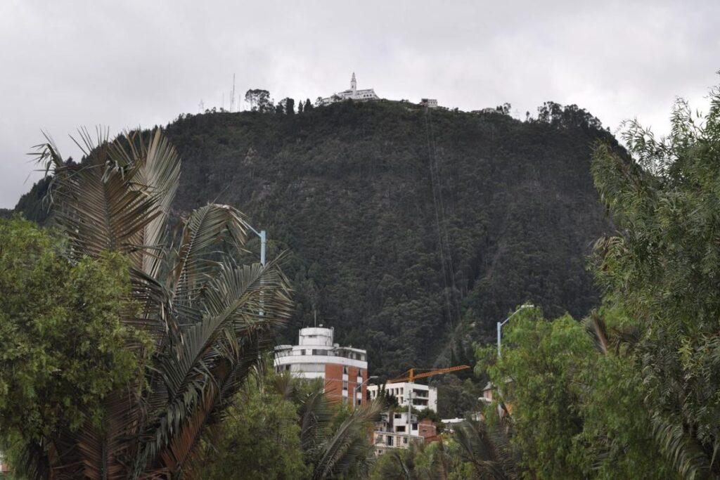 Cerro de Monserrate coberto por vegetação, com o santuário no topo e construções de Bogotá em primeiro plano.