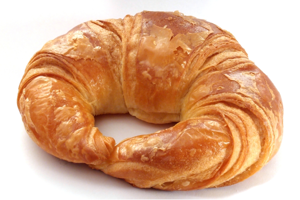 Croissant de manteiga inteiro sobre fundo branco, com camadas folhadas visíveis