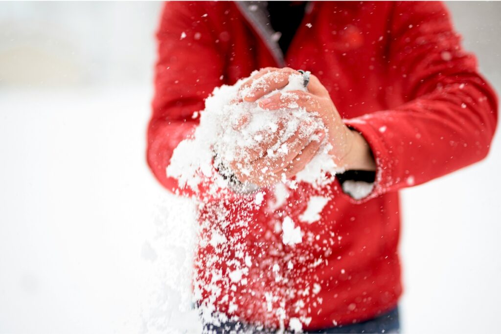 Pessoa com casaco vermelho segurando neve entre as mãos durante o inverno em Bariloche.