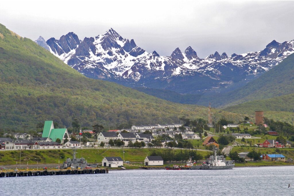 Vista de Puerto Williams, no Chile, com construções, embarcações e montanhas nevadas ao fundo.