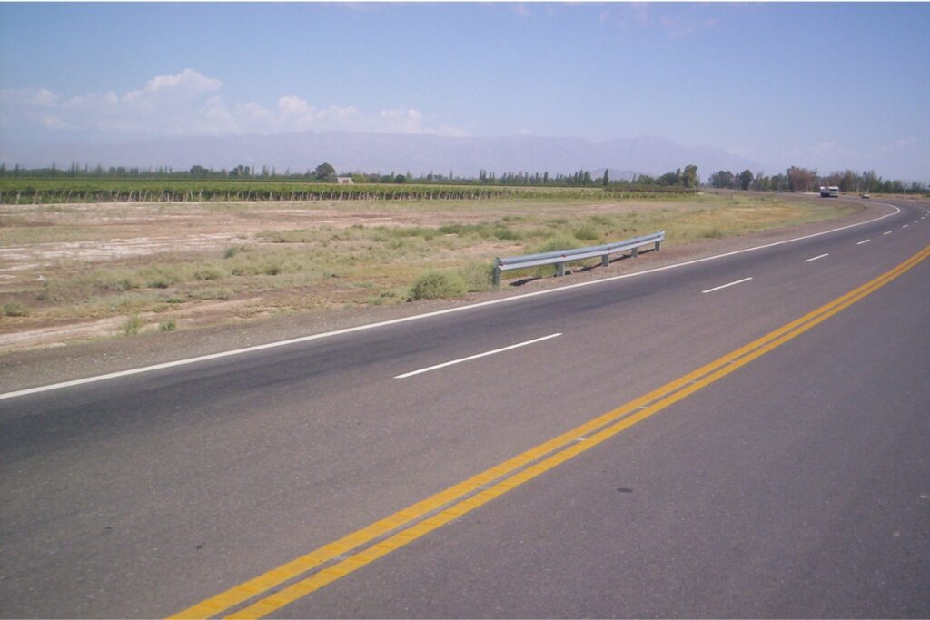 Rodovia asfaltada atravessa uma área rural com plantações e montanhas ao fundo, na Argentina.